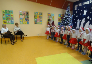 Grupa dzieci wraz z panią dyrektor Marią Królikowska i panią Agnieszką Piekarską śpiewają kolędy.
